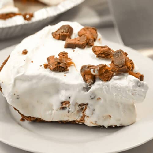A slice of creamy caramel pie topped with crumbled chocolate pieces on a white plate.