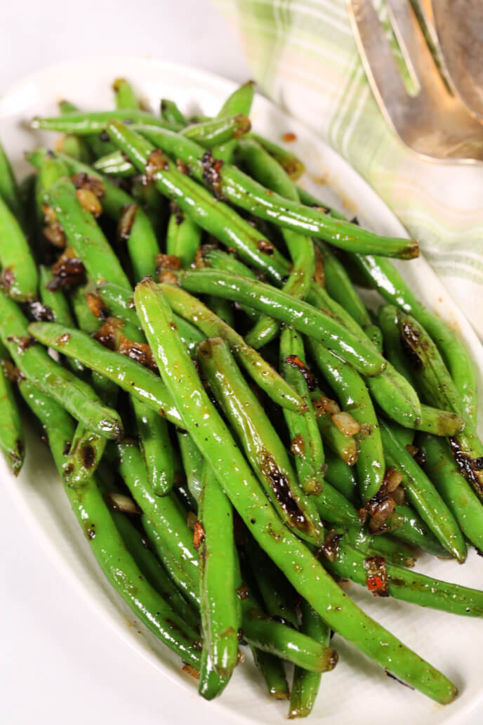 Sweet and spicy green beans on a white plate with a green plaid napkin