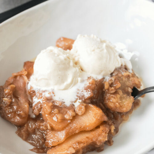 A white bowl of peach cobbler with ice cream.