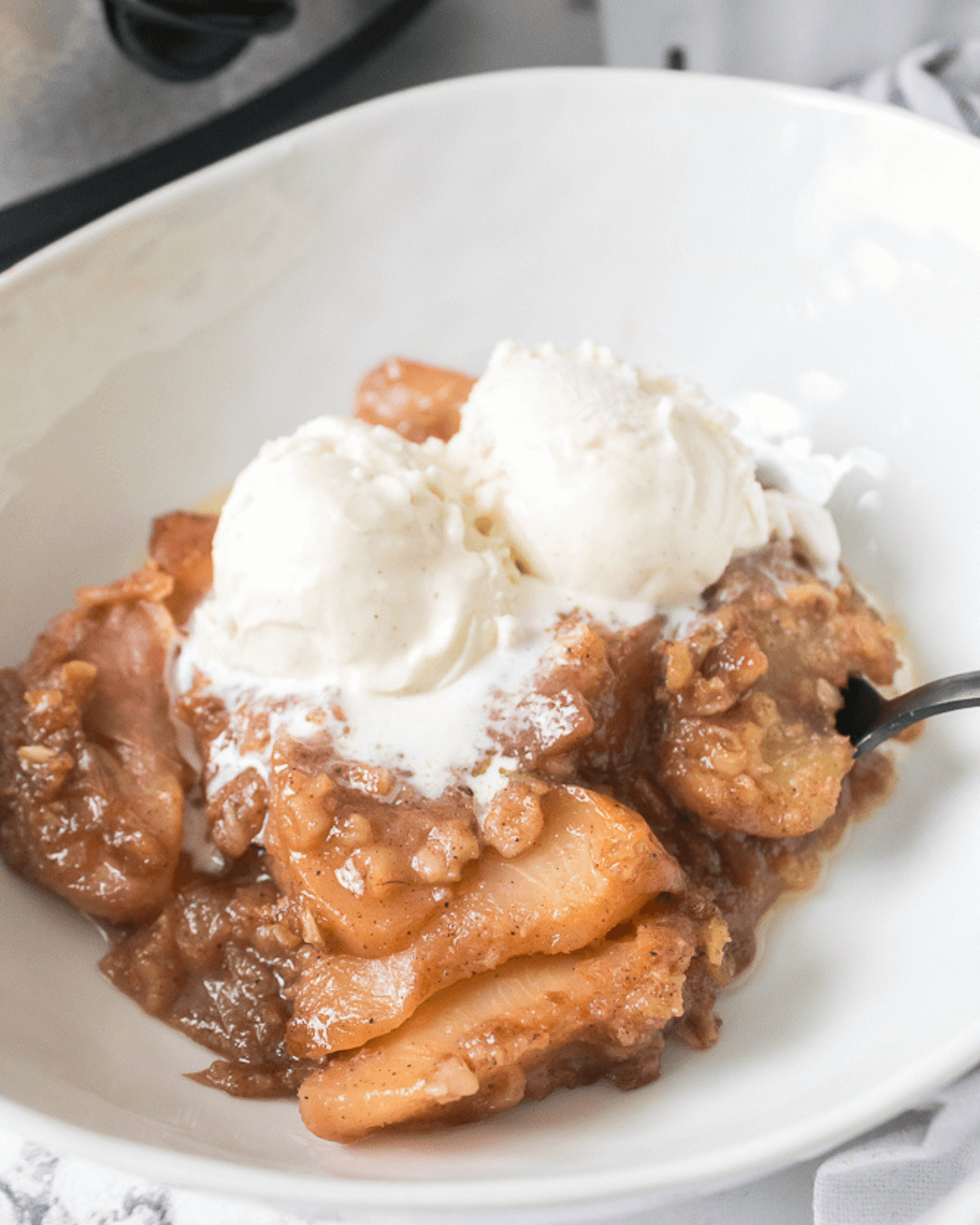 A white bowl of peach cobbler with ice cream.
