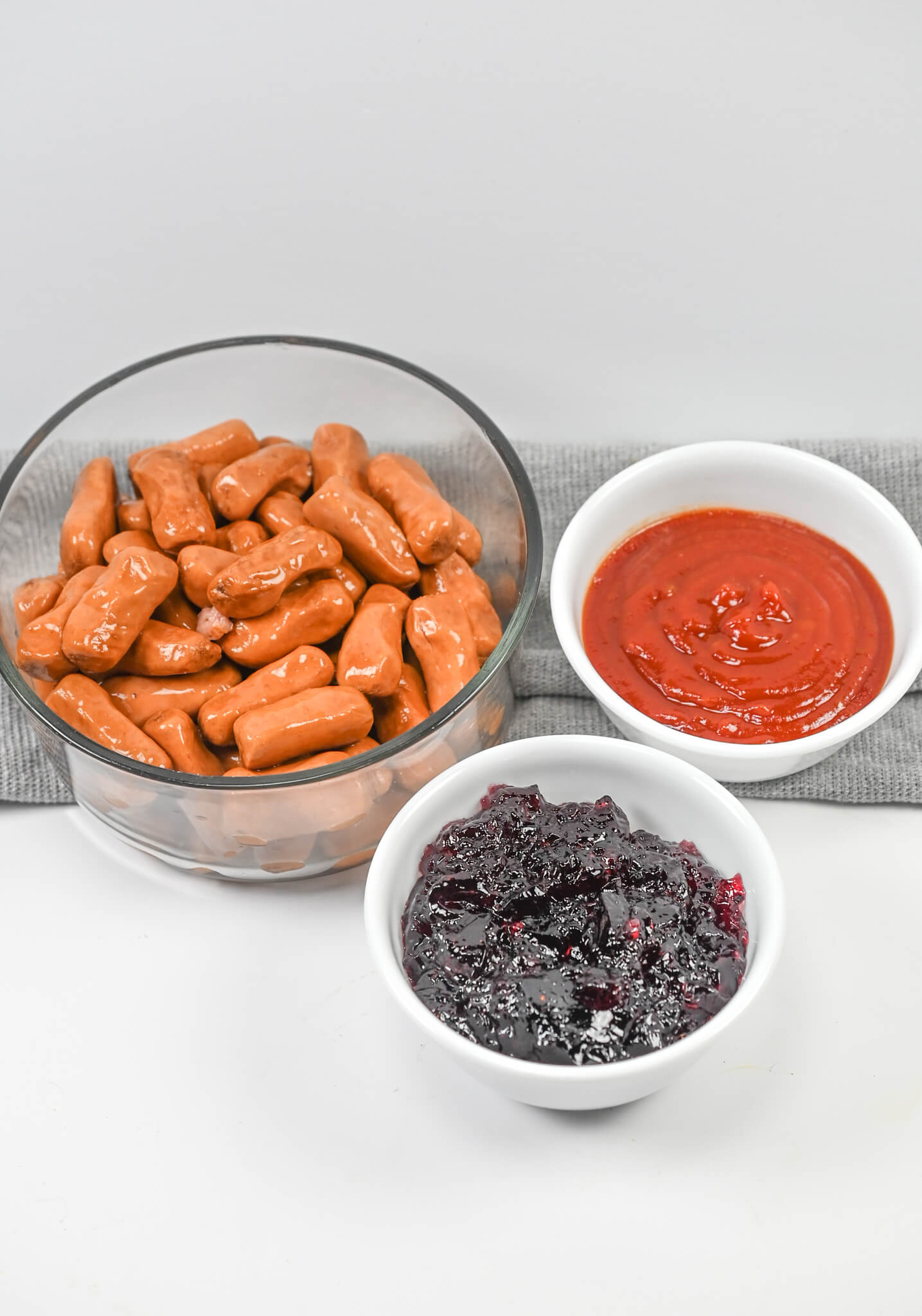 A bowl of ketchup, a bowl of sauce, and a bowl of hot dogs and jelly.