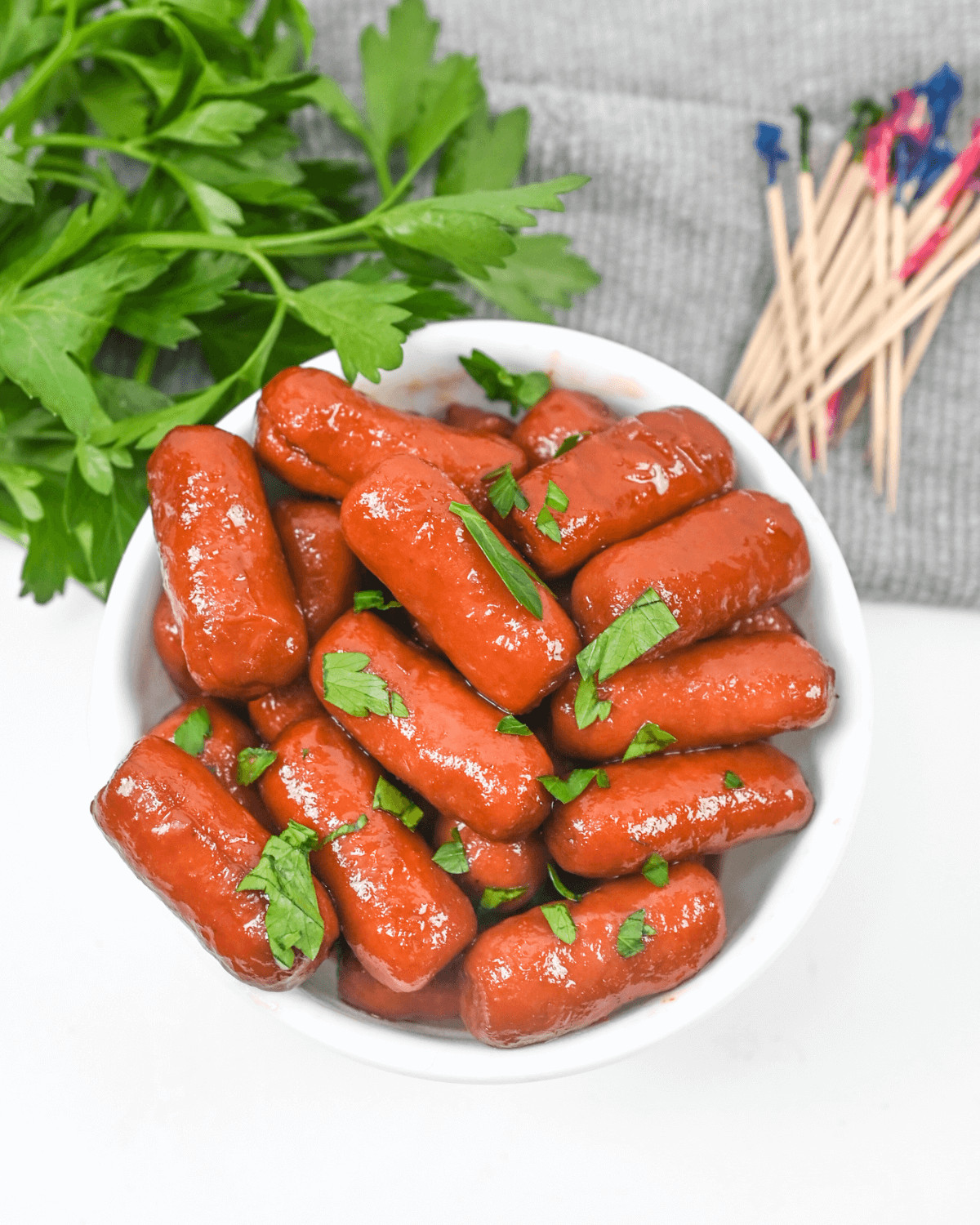 Crock pot little smokies recipe served in a bowl with parsley and matchsticks.