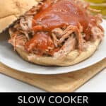 A pulled pork sandwich topped with barbecue sauce on a bun, with pickles in the background. Caption reads "Slow Cooker Dr. Pepper Pulled Pork.