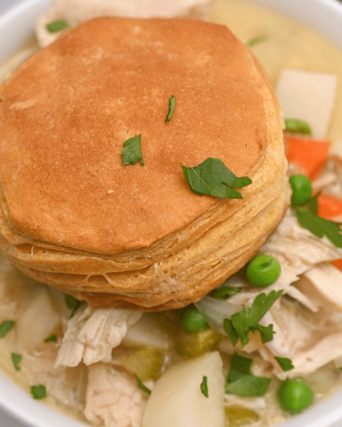 A plate of food with a biscuit and vegetables, including a crockpot chicken pot pie.