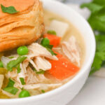 A meal featuring a rich bowl of chicken with a flaky pastry on top.