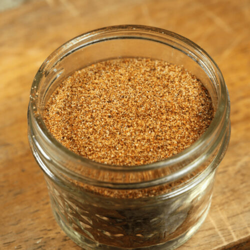 A glass jar filled with low sodium taco seasoning on a wooden surface.