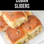 A plate of slow cooker Cuban sliders topped with sesame seeds. The small sandwiches are made with soft rolls, shredded pork, pickles, and melted cheese. A jar is partially visible in the background.