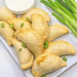 Chicken empanadas served on a white plate with a dip.