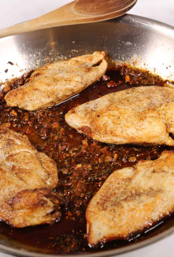 Honey glazed chicken in a skillet with a wooden spoon