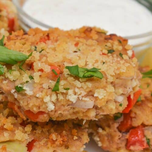 Crispy tuna cakes garnished with herbs on a white plate, served with a small bowl of white dipping sauce in the background.
