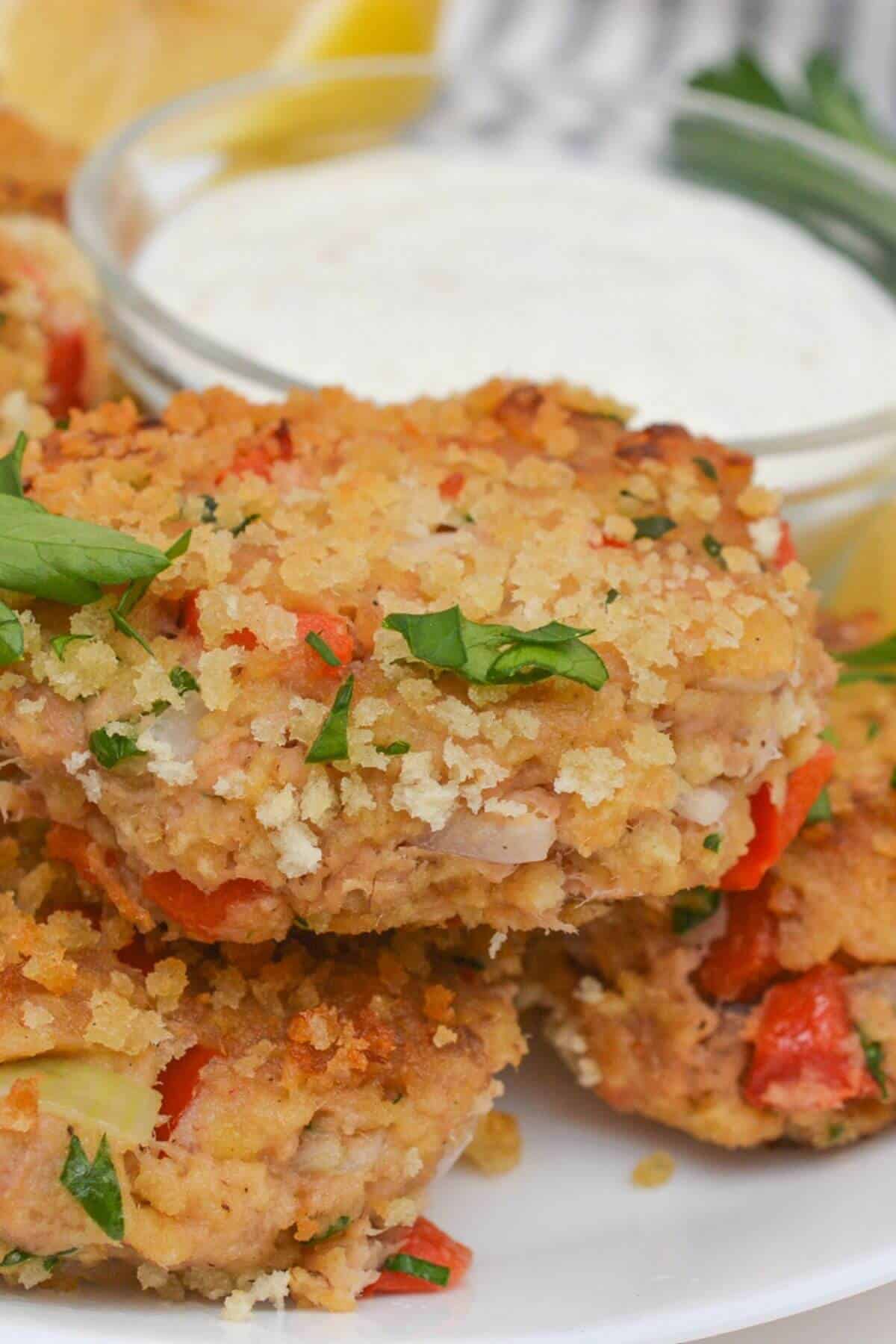 Crispy tuna cakes garnished with herbs on a white plate, served with a small bowl of white dipping sauce in the background.