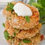 The dish stacked on a plate, garnished with a dollop of white sauce and fresh parsley, with a bowl of sauce in the background.