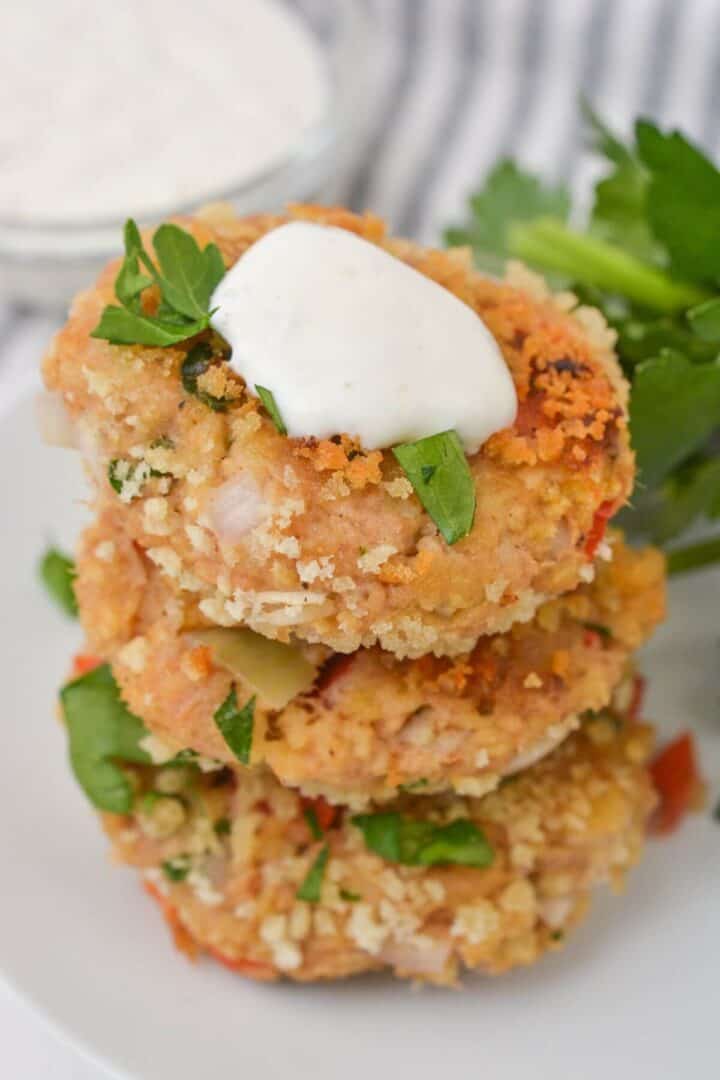 The dish stacked on a plate, garnished with a dollop of white sauce and fresh parsley, with a bowl of sauce in the background.