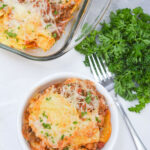 A bowl filled with a serving of the baked ravioli casserole with a side of fresh herbs.