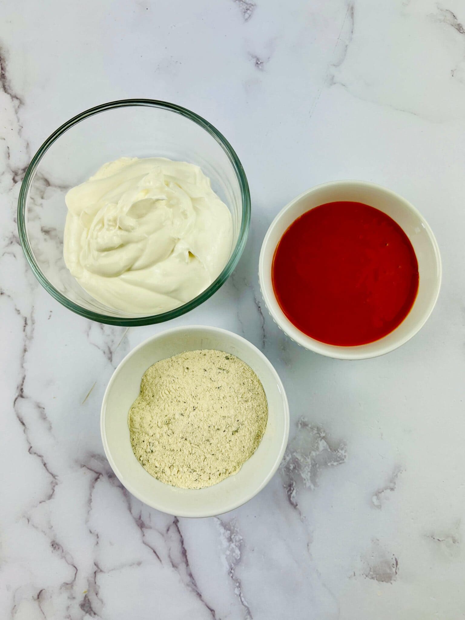 A bowl of ranch, a bowl of hot sauce, and seasoning.