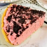 A slice of raspberry cream pie with a graham cracker crust and chocolate cookie crumbs on top, served on a white plate.