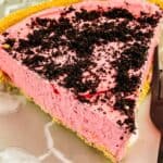 A slice of dessert with a crumbly cookie topping and a graham cracker crust sits on a glass plate next to a fork.