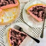 A partially dessert with chocolate crumbs on top, served on two white plates with forks, set on a white patterned cloth and rustic white wooden surface.