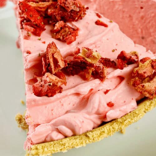 A slice of strawberry pie with graham cracker crust, topped with red crumbled pieces and set in a crumbly crust on a white plate.
