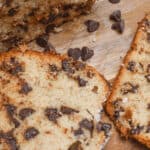 Two slices of chocolate chip banana bread rest on a wooden surface, their rich aroma mingling with scattered chocolate chips.