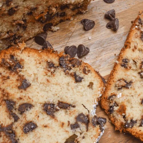 Two slices of chocolate chip banana bread rest on a wooden surface, their rich aroma mingling with scattered chocolate chips.