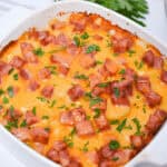 Cheesy Ham and Potato Casserole with melted cheese and diced ham, garnished with parsley, in a white baking dish.