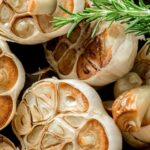 A group of oven roasted garlic cloves with a sprig of rosemary.