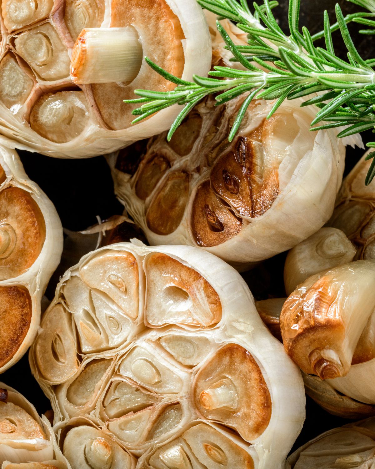 A group of oven roasted garlic cloves with a sprig of rosemary.