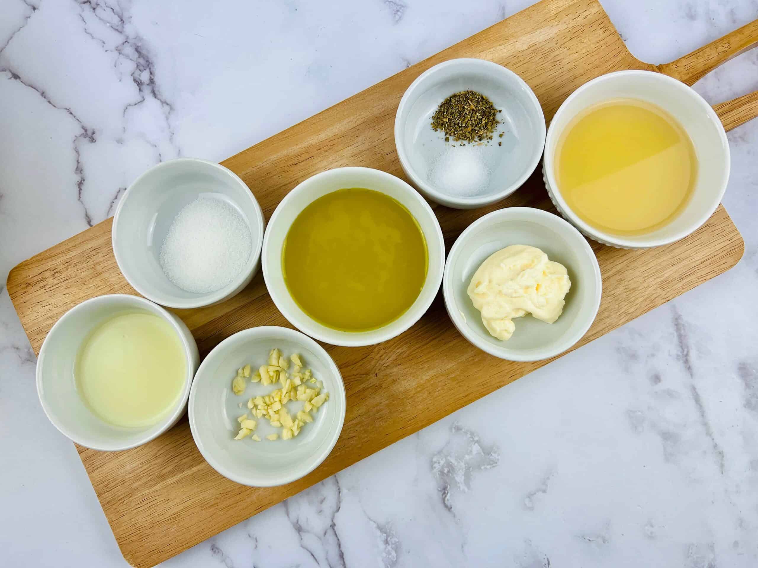 Bowls of ingredients sit on a wooden cutting board for an Italian Chopped Salad.