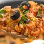 A delicious spoonful of Mexican Beef and Rice Skillet casserole garnished with black olives and fresh herbs, showcasing rice, ground meat, and melted cheese, complemented by a dollop of sour cream on the side.
