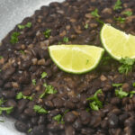 A white dish with slices of lime on top of the mexican black beans.