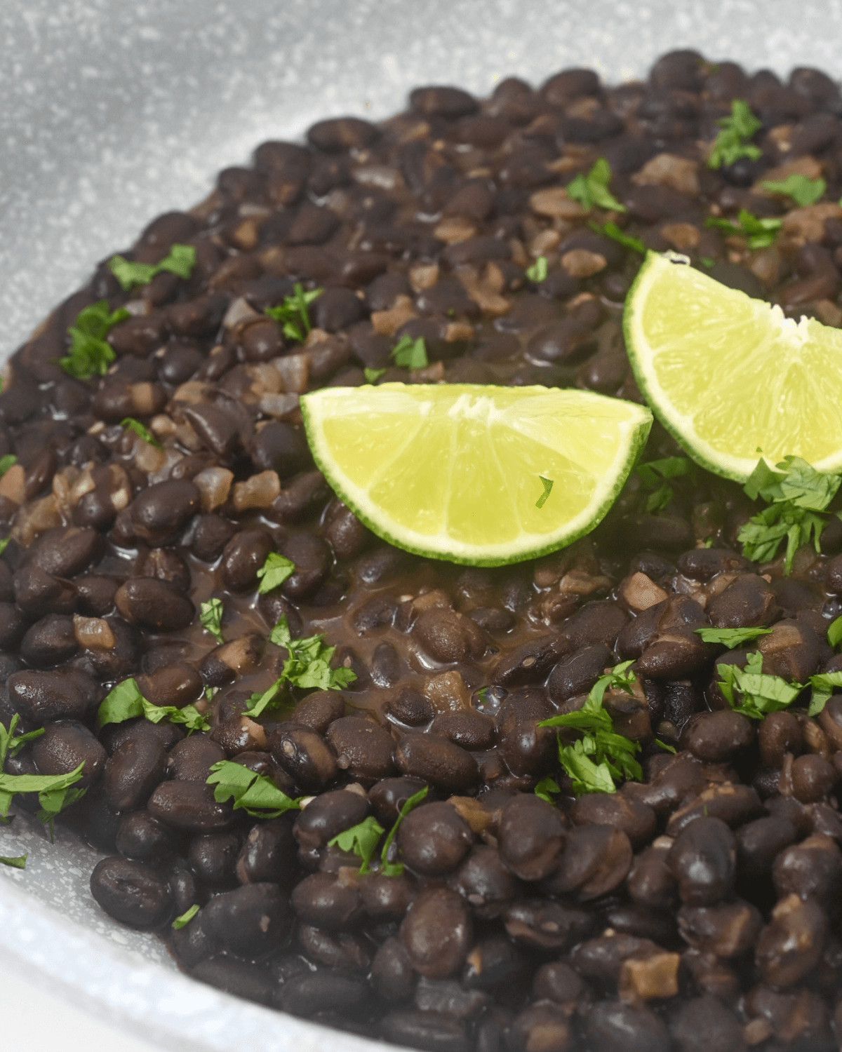A white dish with slices of lime on top of the mexican black beans.