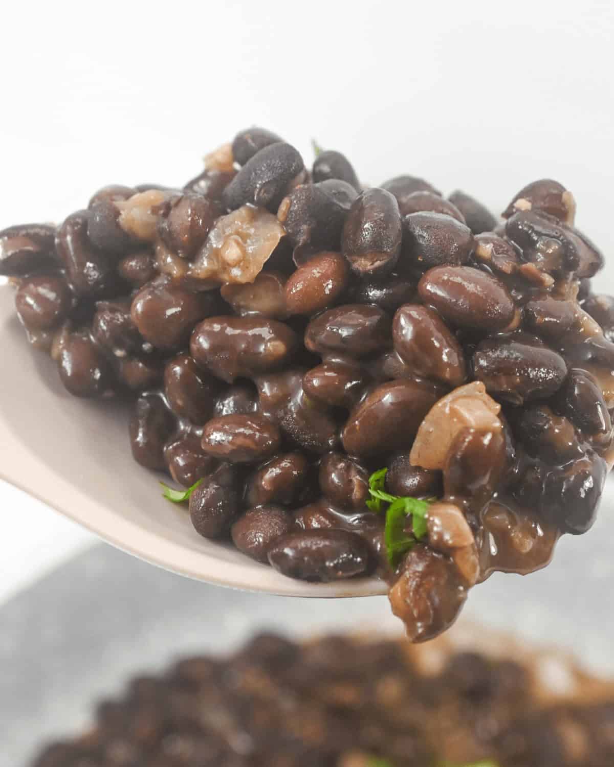 A spoonful of glossy, cooked beans lifted above a bowl, with beans visibly topped with minced onions and herbs.