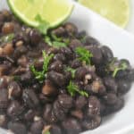 A serving bowl garnished with chopped parsley and lime wedges on the side.