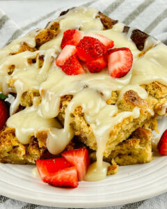 A plate of bread pudding with vanilla sauce topped with fresh strawberry slices.