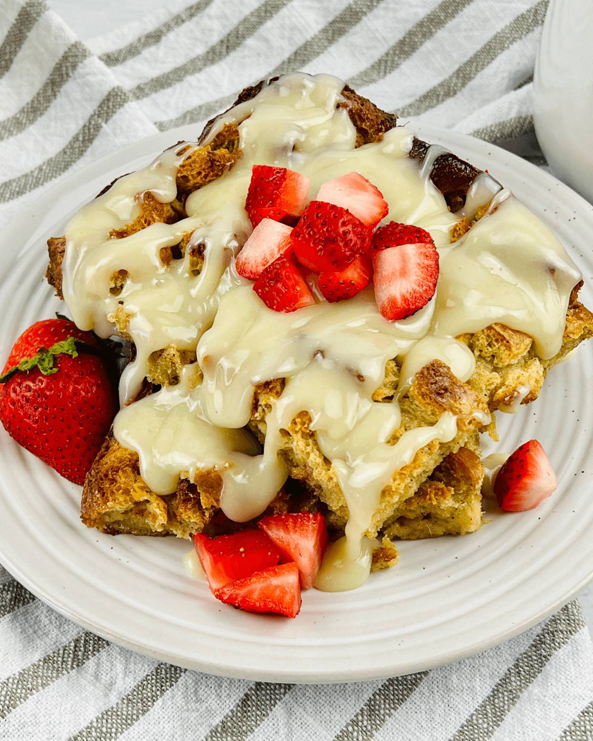 A plate of bread pudding topped with vanilla glaze and fresh strawberries.