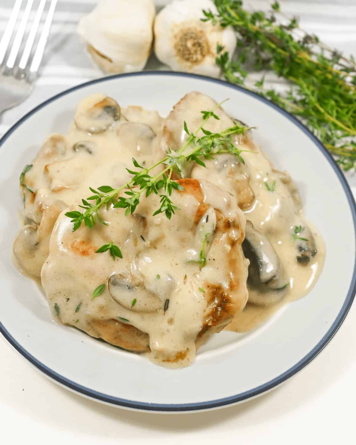 Pork chops with a creamy mushroom sauce garnished with fresh herbs served on a plate.