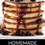 A stack of pancakes drizzled with homemade blueberry syrup, accompanied by fresh blueberries on and around the pancakes. Text at the bottom reads "Homemade Blueberry Syrup".