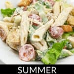 A fresh Caesar pasta salad with penne, croutons, lettuce, and tomatoes, labeled "Summer Caesar Pasta Salad," served on a white plate.