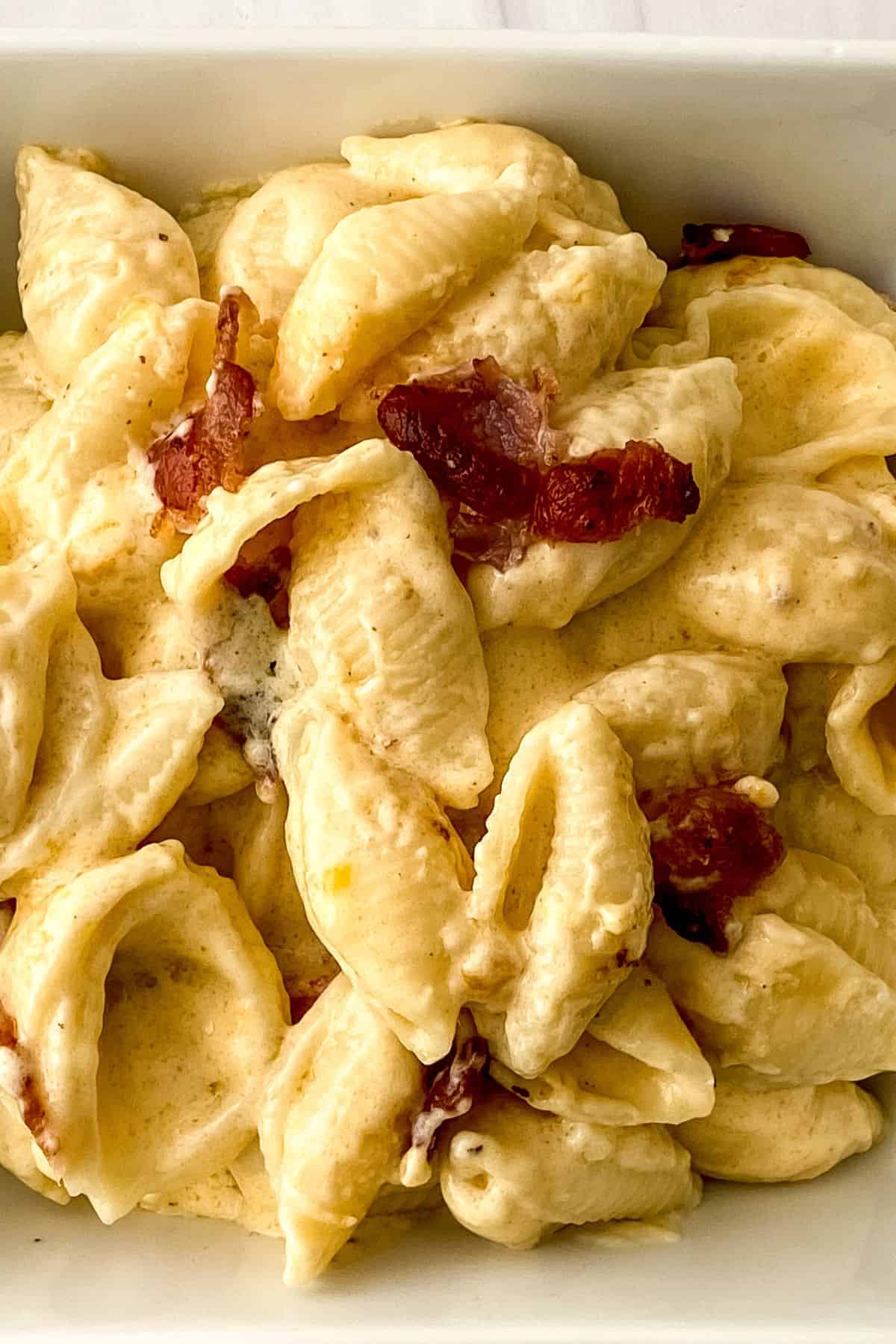 Shell pasta coated in creamy cheese sauce with pieces of crispy bacon, this Bacon Mac and Cheese is served in a white dish.