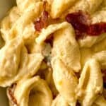 Close-up of Bacon Mac and Cheese featuring pasta shells coated in creamy cheese sauce with pieces of bacon.