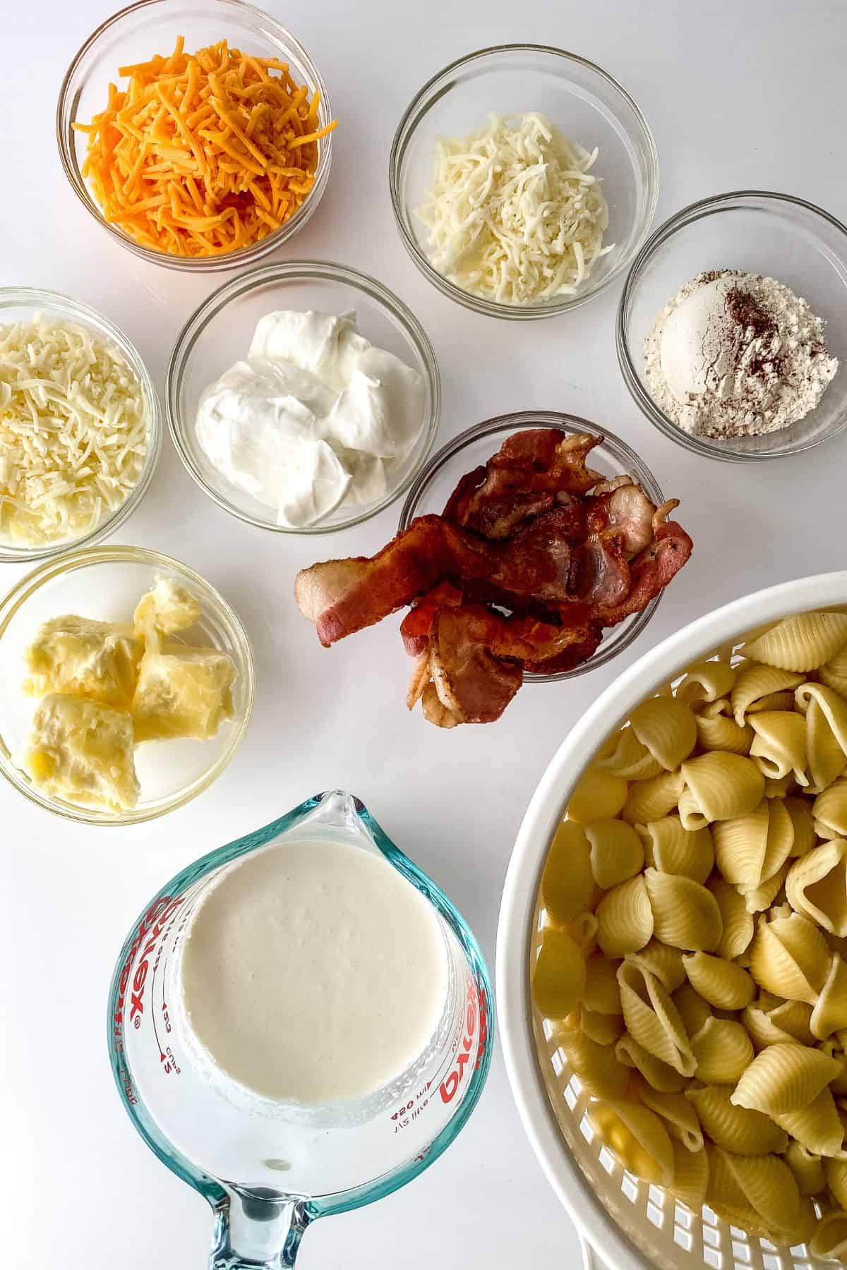 Ingredients  are arranged on a white surface, including cooked shell pasta, crispy meat, butter, flour, and milk.