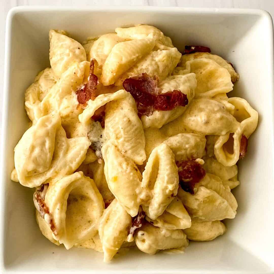 A square white bowl filled with creamy Bacon Mac and Cheese, featuring tender shell pasta and savory pieces of bacon.
