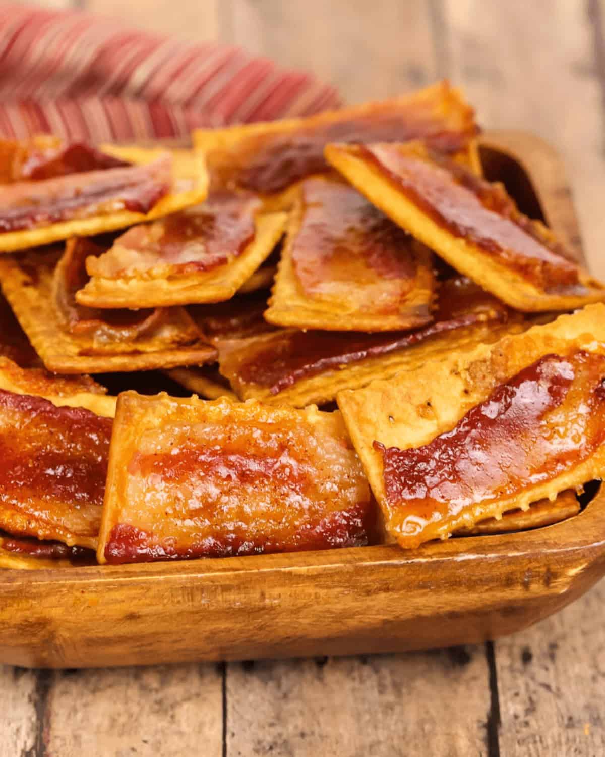 Bacon crackers displayed in a wooden bowl on top of a rustic wooden table.