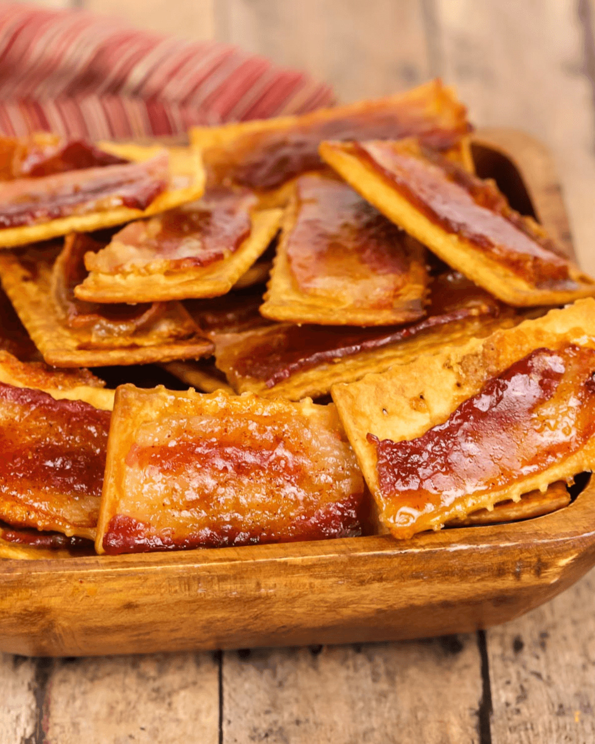 Bacon crackers displayed in a wooden bowl on top of a rustic wooden table.