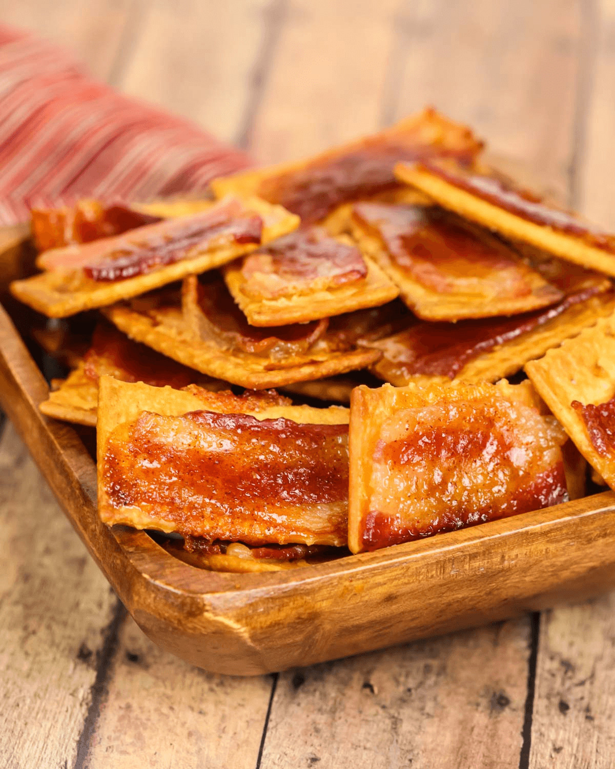 A bowl of glazed bacon crackers on a wooden table.