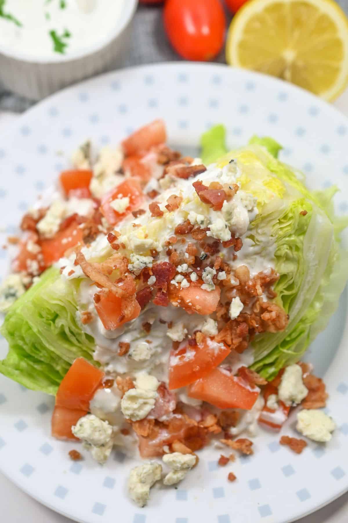 An meal features a crisp wedge of iceberg lettuce topped with diced tomatoes, bacon bits, blue cheese crumbles, and creamy dressing, all beautifully arranged on a white plate.