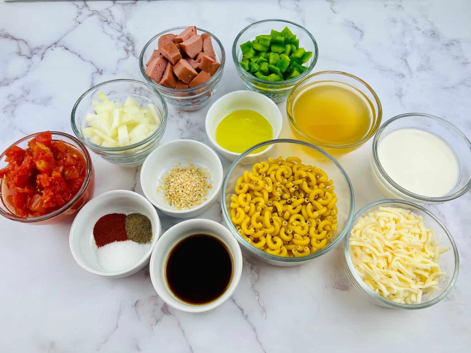 On the marble table, there are ingredients  of noodles, sausage, tomatoes and seasoning.