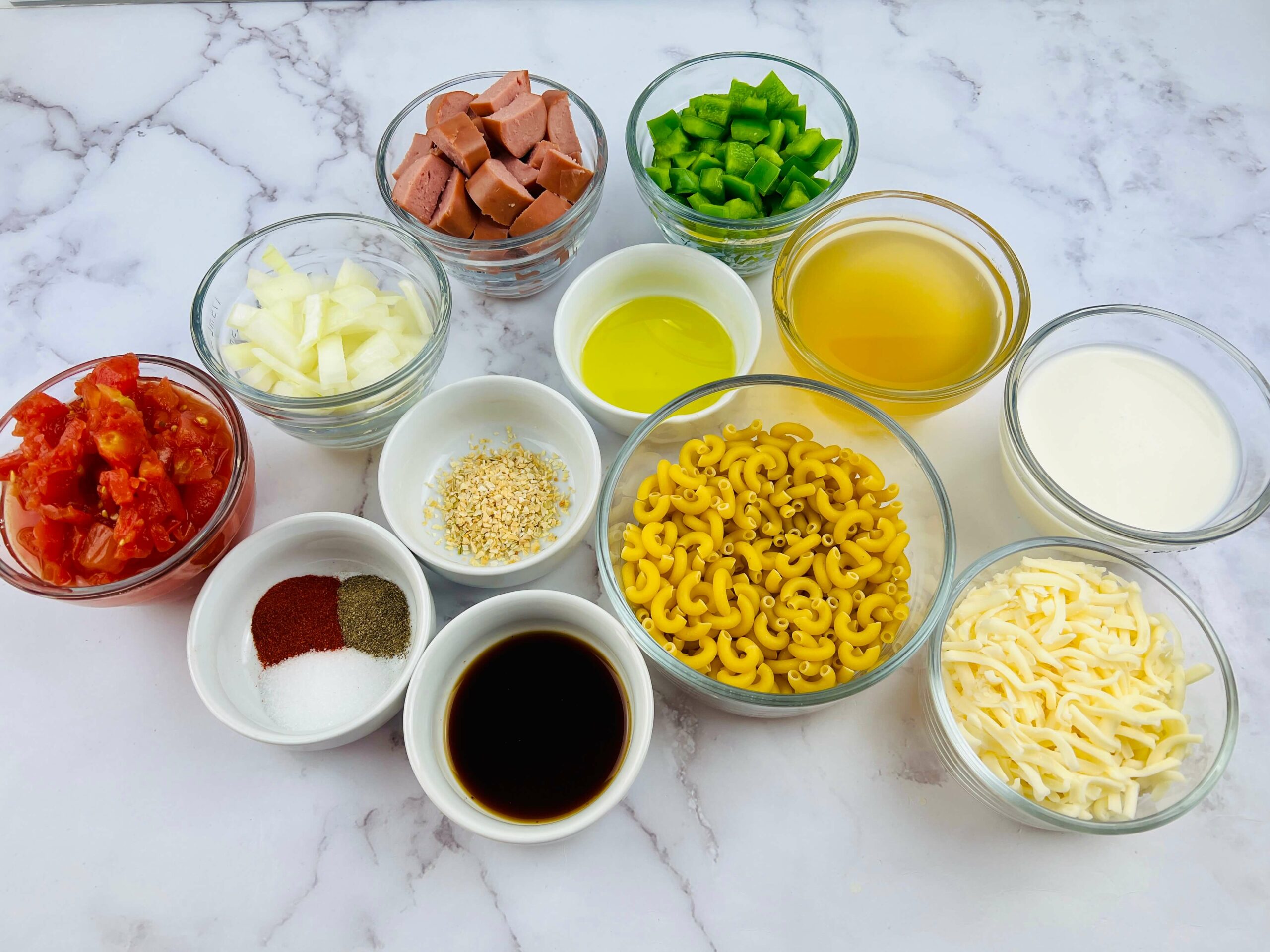 On the marble table, there are ingredients  of noodles, sausage, tomatoes and seasoning.