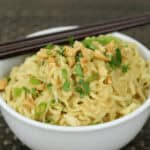 A bowl garnished with chopped peanuts and green onions, with chopsticks resting on the rim.